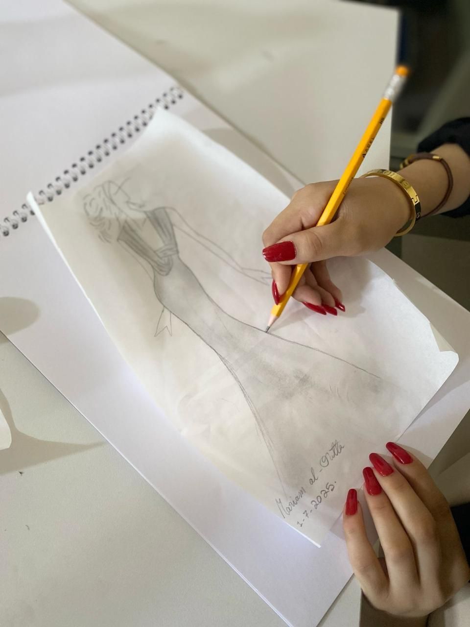 يد متدرّبة ترسم تصميماً لفستان بقلم رصاص ضمن دورة الخياطة