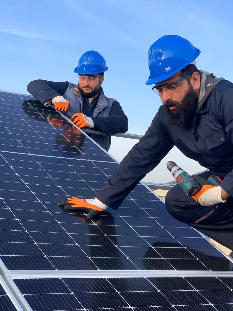 متدرّبان بخوذتين زرقاوين يركّبان لوح طاقة شمسية على السطح